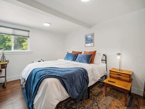 A bedroom with a bed, a nightstand, a lamp, a window, and a framed picture on the wall. - The Hartson  Vintage Charm on the Ben Burr Trail (Spokane)