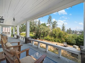 Une terrasse couverte, aménagée avec du mobilier d’extérieur, une cheminée en pierre et une vue sur un jardin paysager.