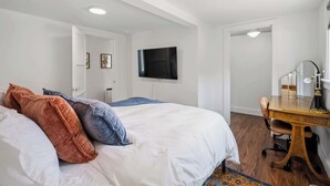 A bedroom with a bed, a desk, a chair, a television, and a mirror.