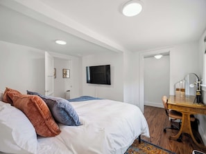 A bedroom with a bed, a desk, a chair, a television, and a mirror.