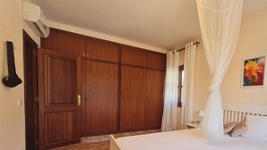 Un dormitorio con cama, armario, mesita de noche y ventana con cortinas.