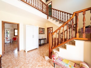 Ein mehrstöckiges Interieur mit einer Holztreppe, einem Essbereich mit roten Stühlen, einem weißen Schrank und einem farbenfrohen Sofa.