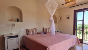 Un dormitorio con una cama grande, una mesita de noche, una lámpara, una cama con dosel y vistas a través de una puerta de vidrio.