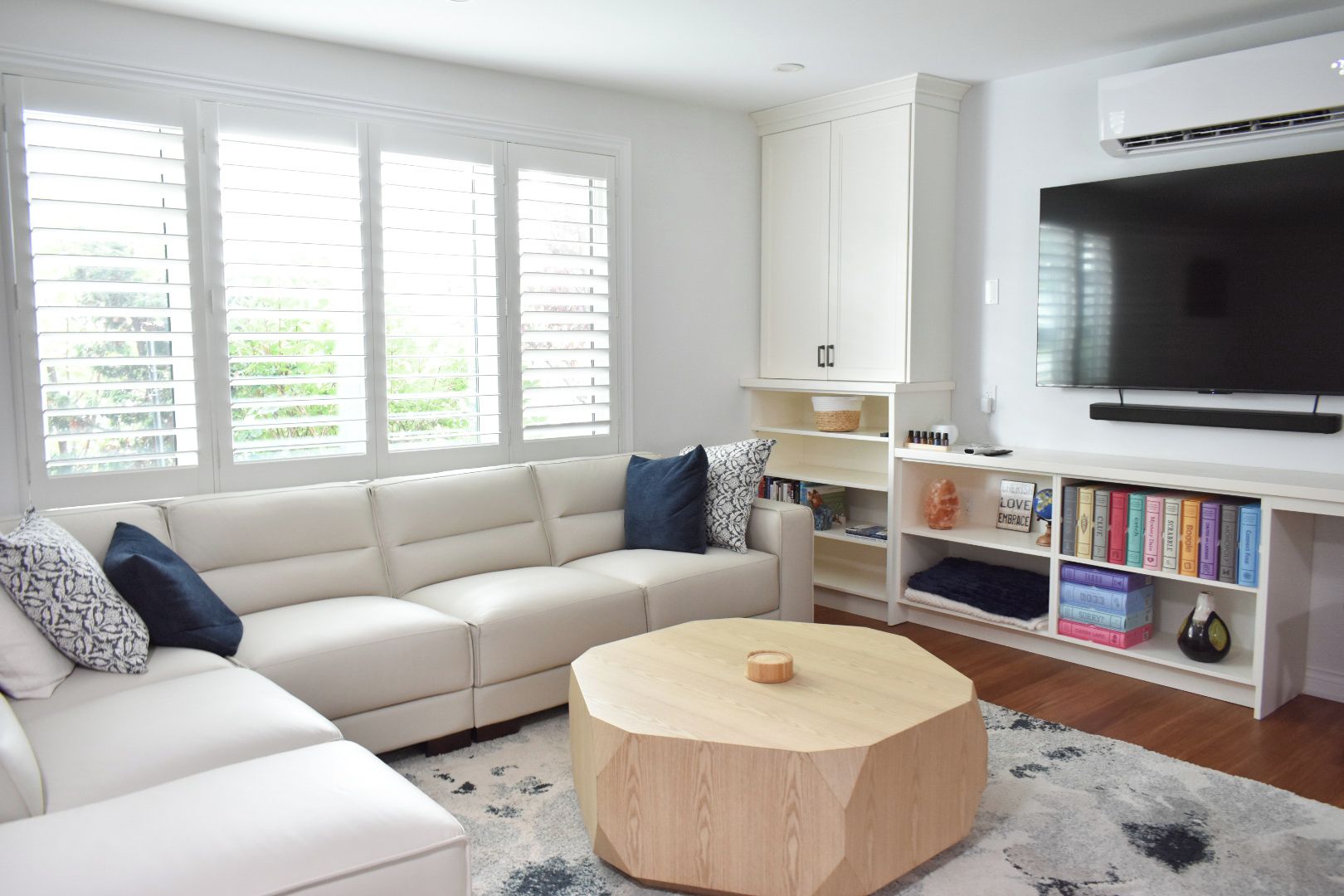 A modern living room with a white sofa, a round coffee table, a bookshelf, and a flat-screen TV.