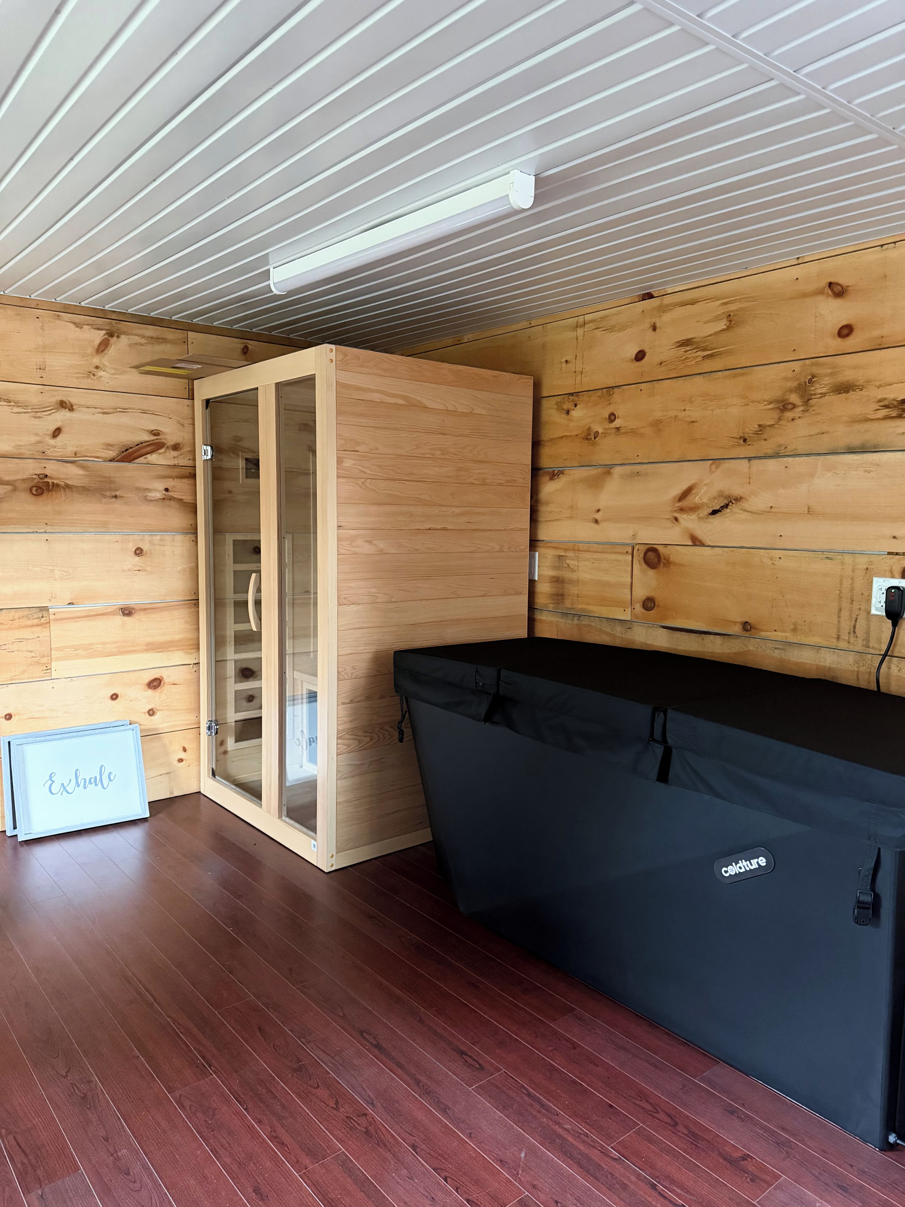 A room with wooden walls, a glass door, a black sofa, and a wooden floor.