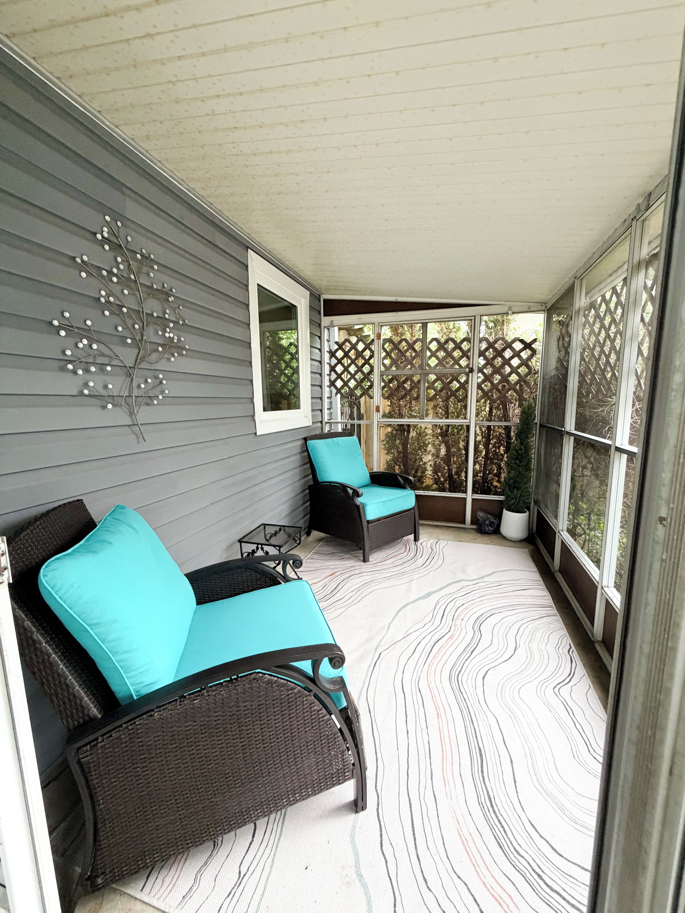 A covered porch with two wicker chairs, a small table, and a decorative wall piece.