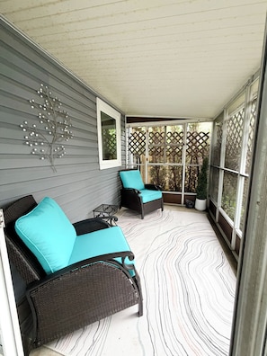 A covered porch with two wicker chairs, a small table, and a decorative wall piece.