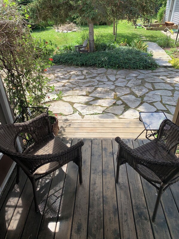 A wooden deck with wicker chairs and a small table, overlooking a stone pathway and garden.