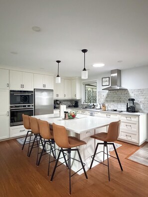 A modern kitchen with white cabinetry, stainless steel appliances, and a central island with bar stools. - The Athlete Retreat / Sauna / Cold plunge / red light / huge kitchen (Port Colborne)