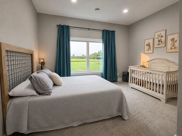 A bedroom with a bed, a crib, a window with curtains, and wall art.