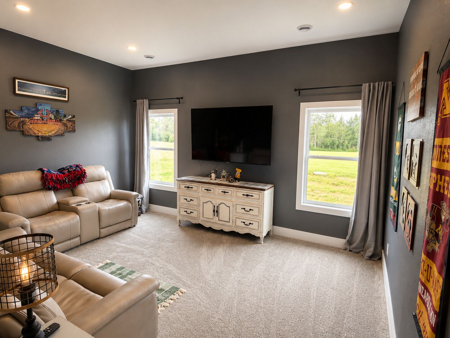 A living room with a beige sofa, a white entertainment center, a flat-screen TV, and large windows with curtains.