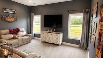 A living room with a beige sofa, a white entertainment center, a flat-screen TV, and large windows with curtains.