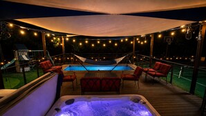 Ett bubbelbad med en trädeck runt om, omgivet av röda stolar och en pool.