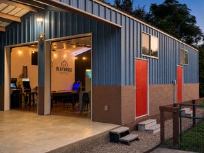 A building with a playhouse sign, a red door, and a staircase leading to the entrance. - The Playhouse | Your Own Private Family Fun Resort (Bastrop)
