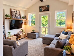 A living room with a flat-screen TV, grey sofas, a coffee table, and a bookshelf. - 3-bedroom bungalow in welcoming downtown Fenton on the Shiawassee River. (Fenton)