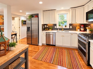 A modern kitchen with white cabinets, stainless steel appliances, and a colorful striped rug. - 3-bedroom bungalow in welcoming downtown Fenton on the Shiawassee River. (Fenton)