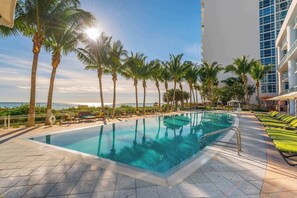 A swimming pool with a view of the ocean, surrounded by palm trees and lounge chairs.