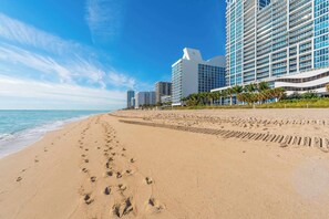 A beach with footprints leading to a building with a clock tower.