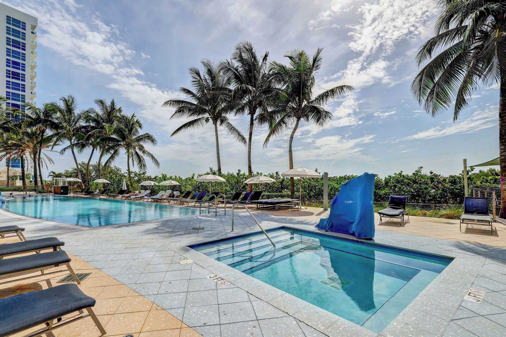 A pool area with lounge chairs, umbrellas, and palm trees.
