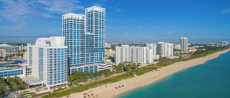 A coastal cityscape with high-rise buildings, a beach, and clear skies.