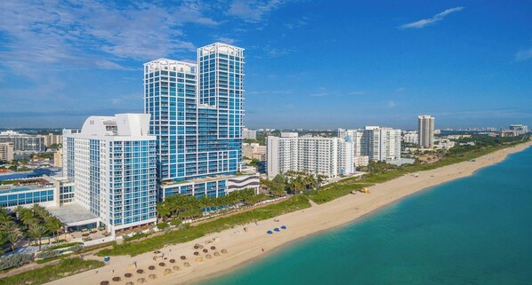A coastal cityscape with high-rise buildings, a beach, and clear skies.