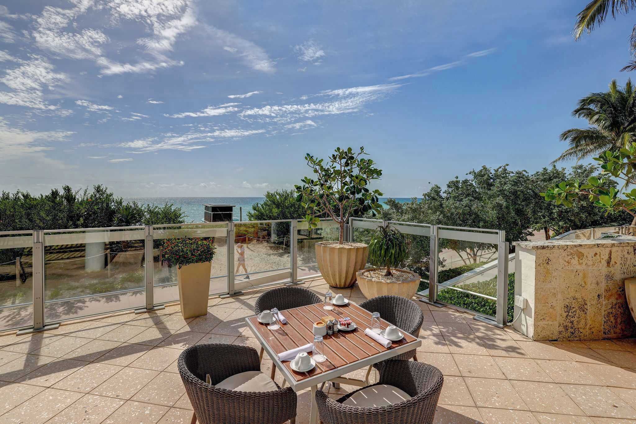 An outdoor dining area with a view of the sea, wicker furniture, and potted plants.