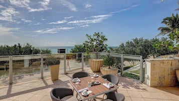 An outdoor dining area with a view of the sea, wicker furniture, and potted plants.