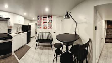 A compact kitchen with modern appliances, a dining area with a table and chairs, and a staircase leading to another level.