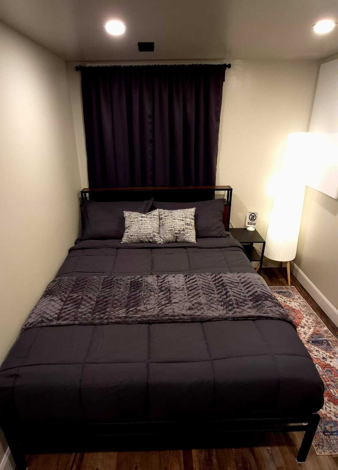 Ein Bett mit dunklem Kopfteil, einer gemusterten Tagesdecke und einem Teppich auf Holzboden.