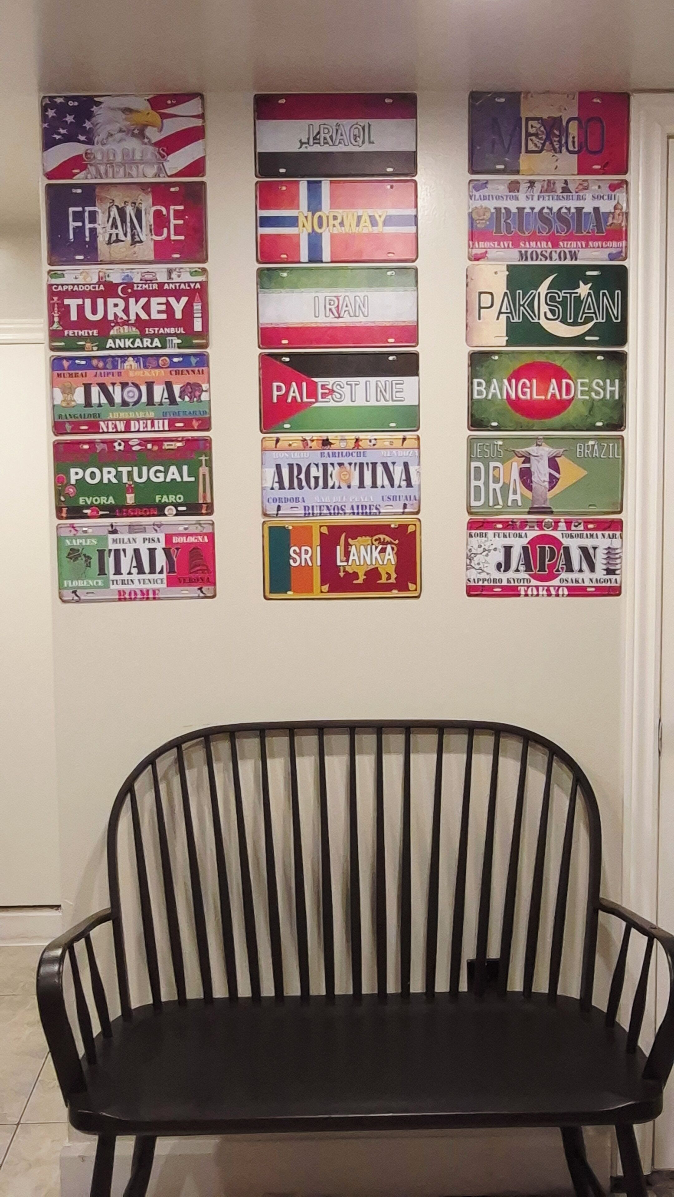 A wall with various country flags and a black metal bench in front.