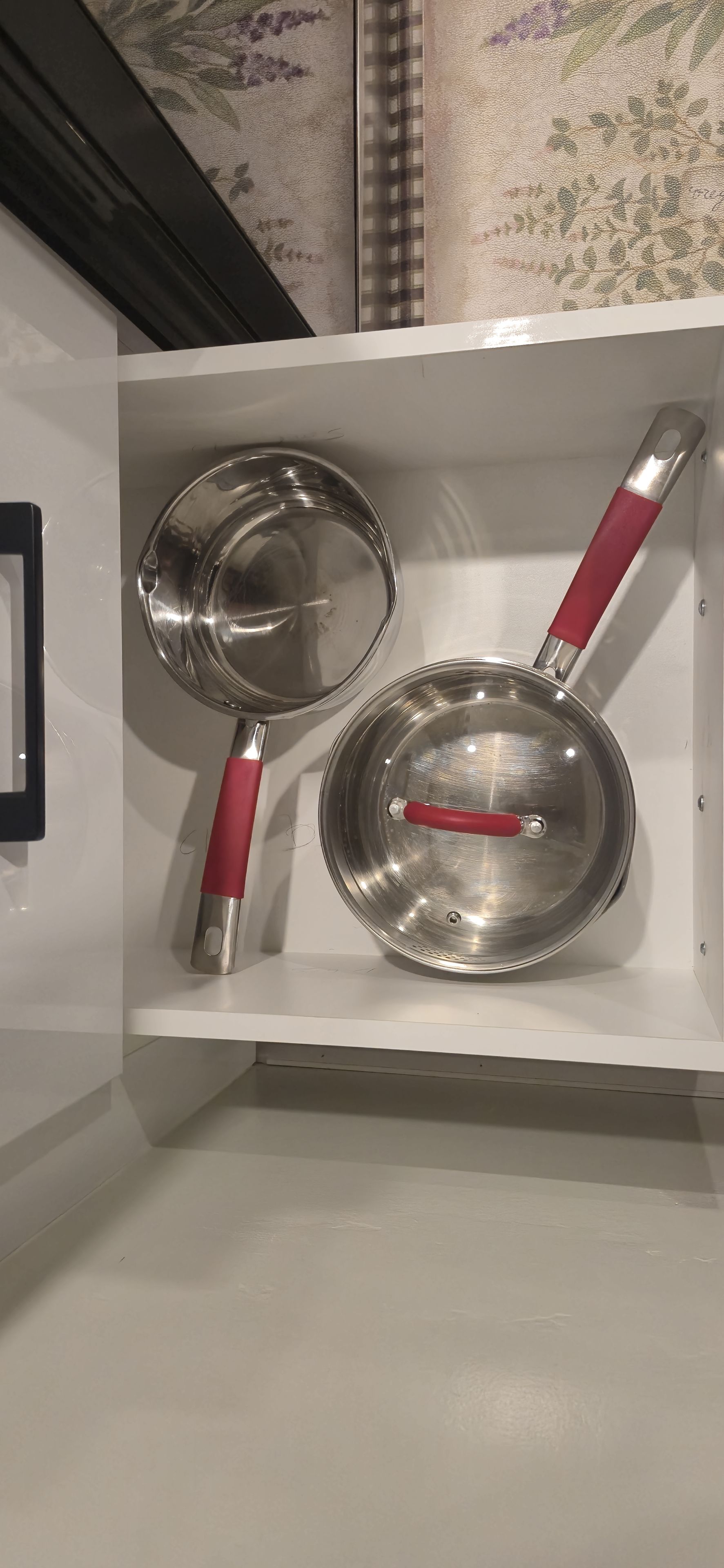 A kitchen utensil drawer with two stainless steel pans and a ladle.
