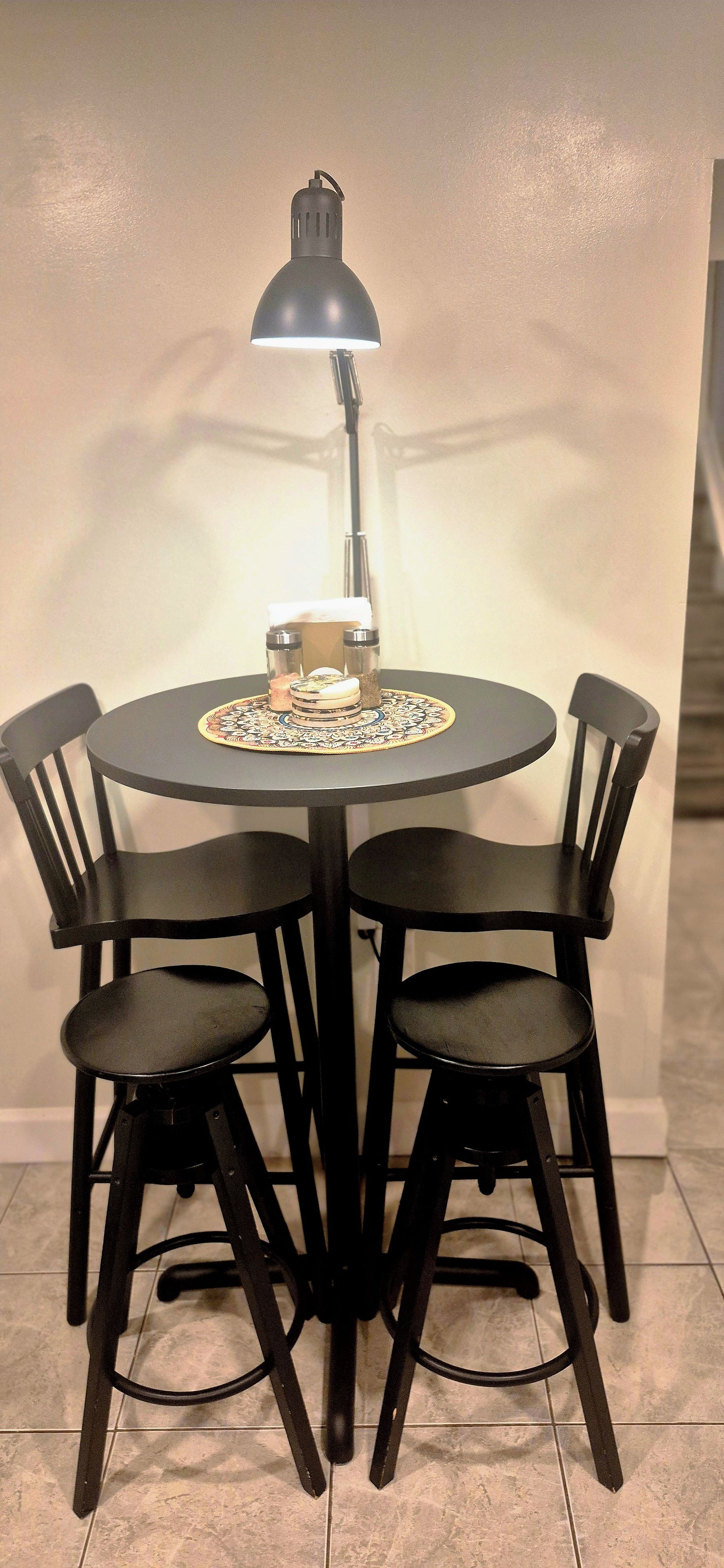 A round dining table with four black chairs, a black table lamp, and a decorative plate.