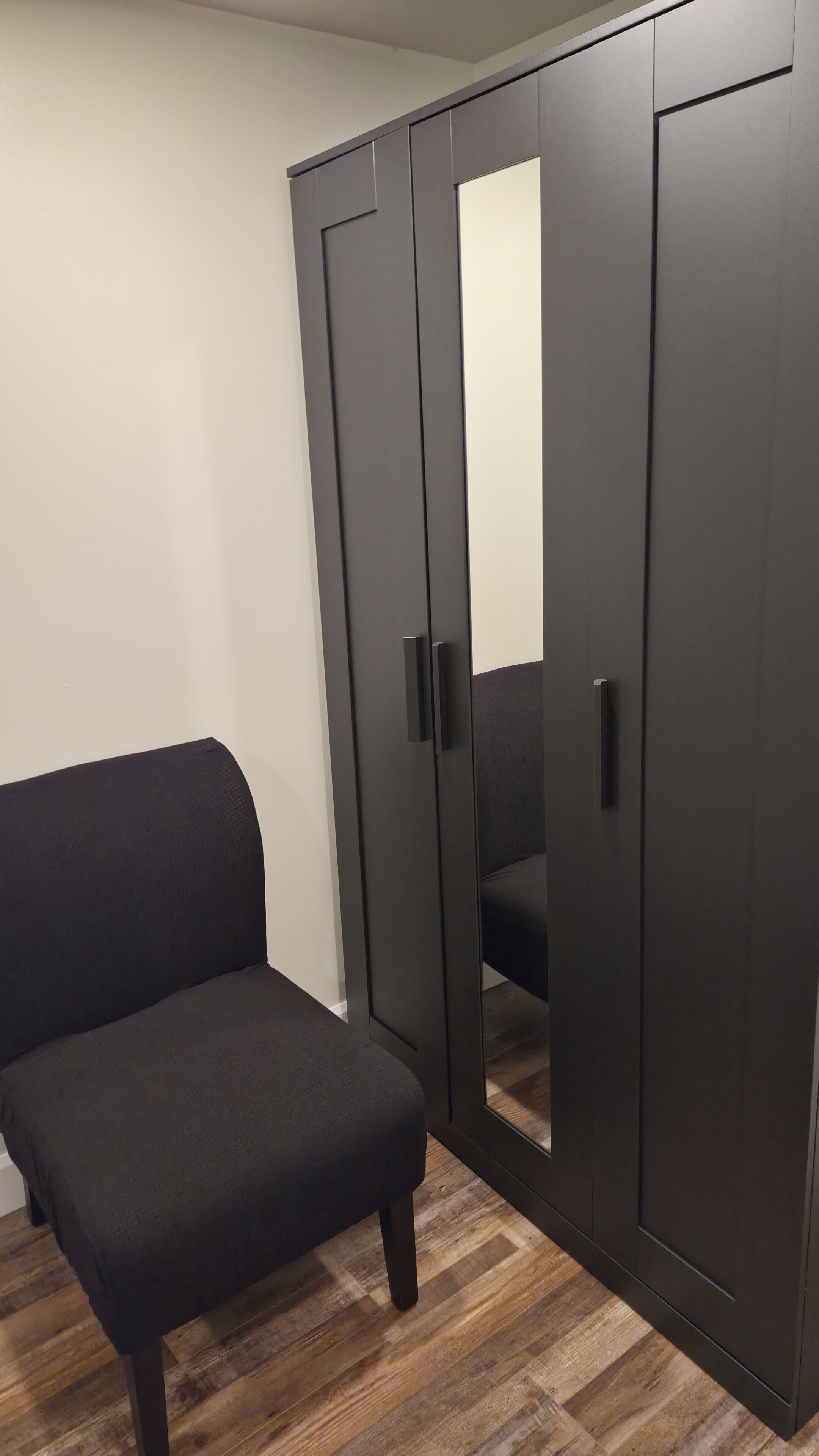 A room with a dark-colored wardrobe, a matching bench, and a wooden floor.