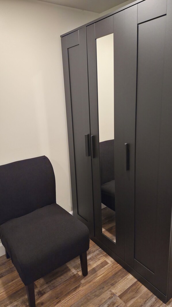 A room with a dark-colored wardrobe, a matching bench, and a wooden floor.