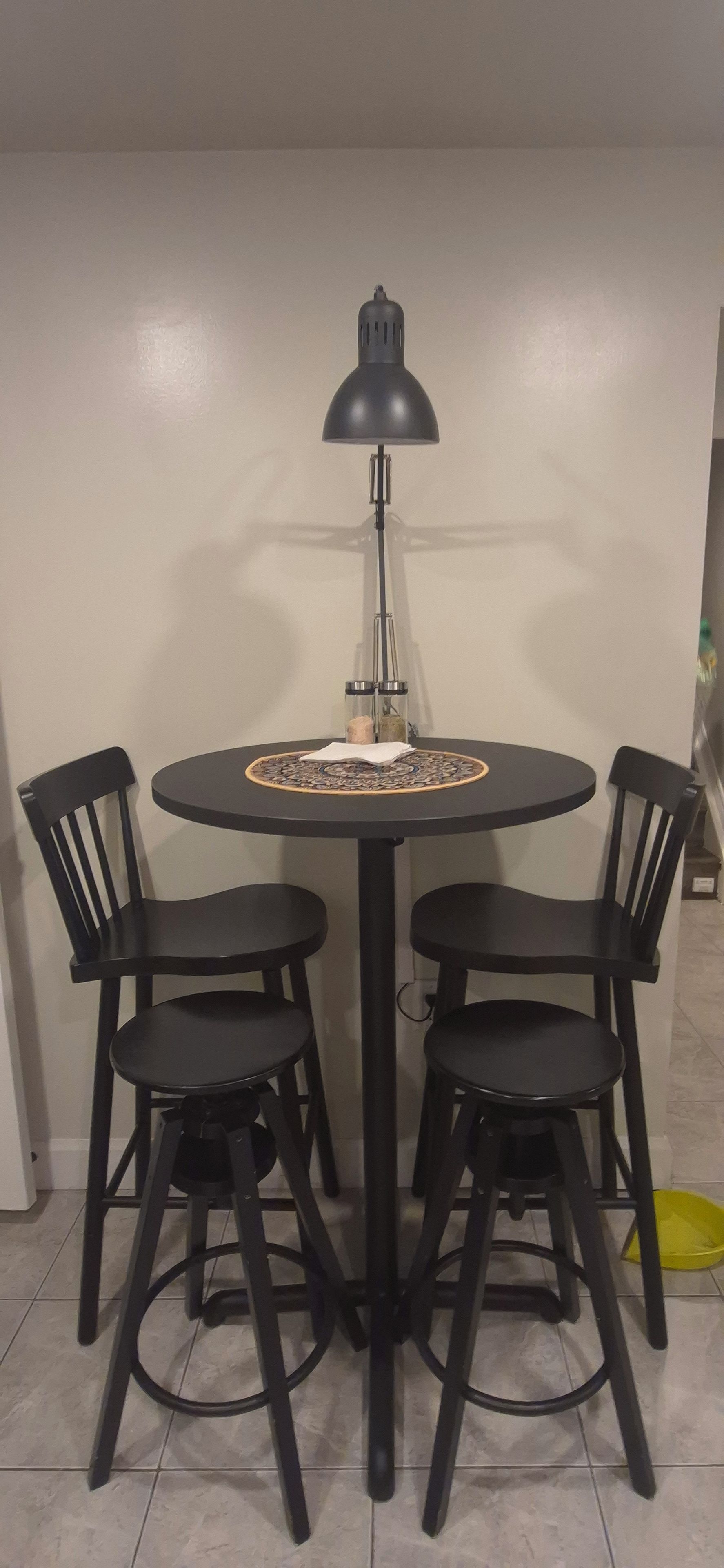 A round dining table with four black chairs, a black table lamp, and a decorative table runner.