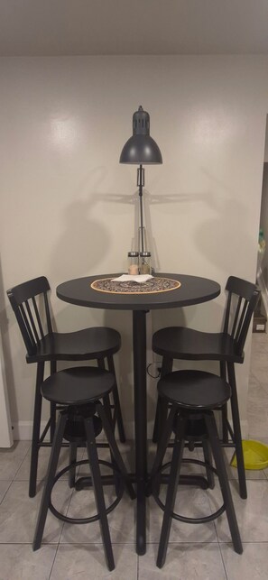 A round dining table with four black chairs, a black table lamp, and a decorative table runner.