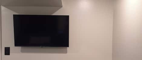 A room with a flat-screen TV mounted on the wall, a black chair, and a wooden floor.