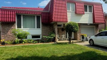 A two-story house with a brick facade, red roof, and a front yard with a lawn and potted plants.