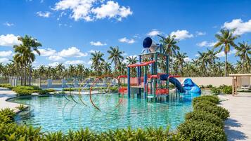 Une piscine avec un toboggan et une aire de jeux, entourée de palmiers et sous un ciel dégagé.