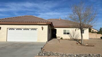 A single-story house with a garage, a small front yard with a tree, and a clear sky.