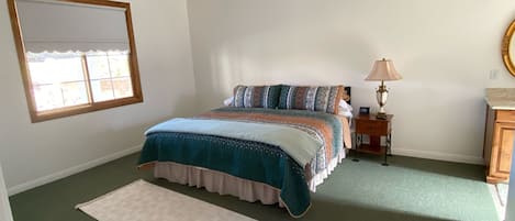 A bedroom with a bed, a ceiling fan, a nightstand, a lamp, a mirror, and a window.