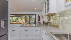 A modern kitchen with white cabinetry, a built-in sink, and a view of the outdoors. - Samsara in Suffolk Park (Suffolk Park)