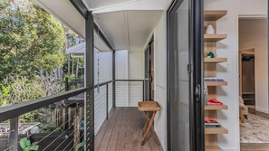 Ein Balkon mit Holzboden, einem kleinen Korbstuhl und einem Bücherregal mit Büchern.