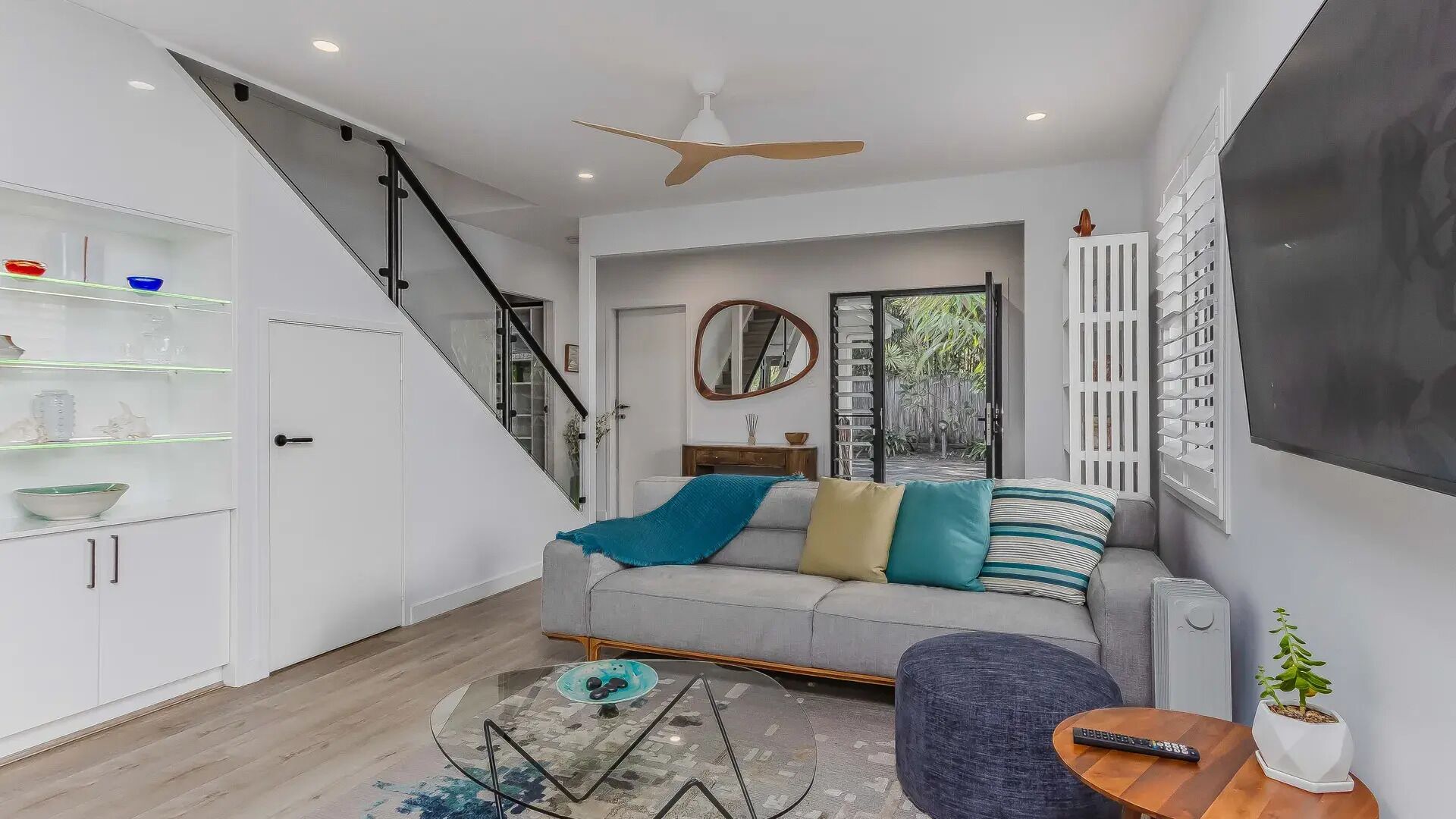 Uma sala de estar moderna com escada, um sofá com almofadas, uma mesa de centro e uma televisão.