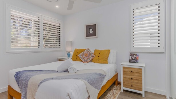 Un dormitorio con cama, mesita de noche, lámpara y un cuadro en la pared.