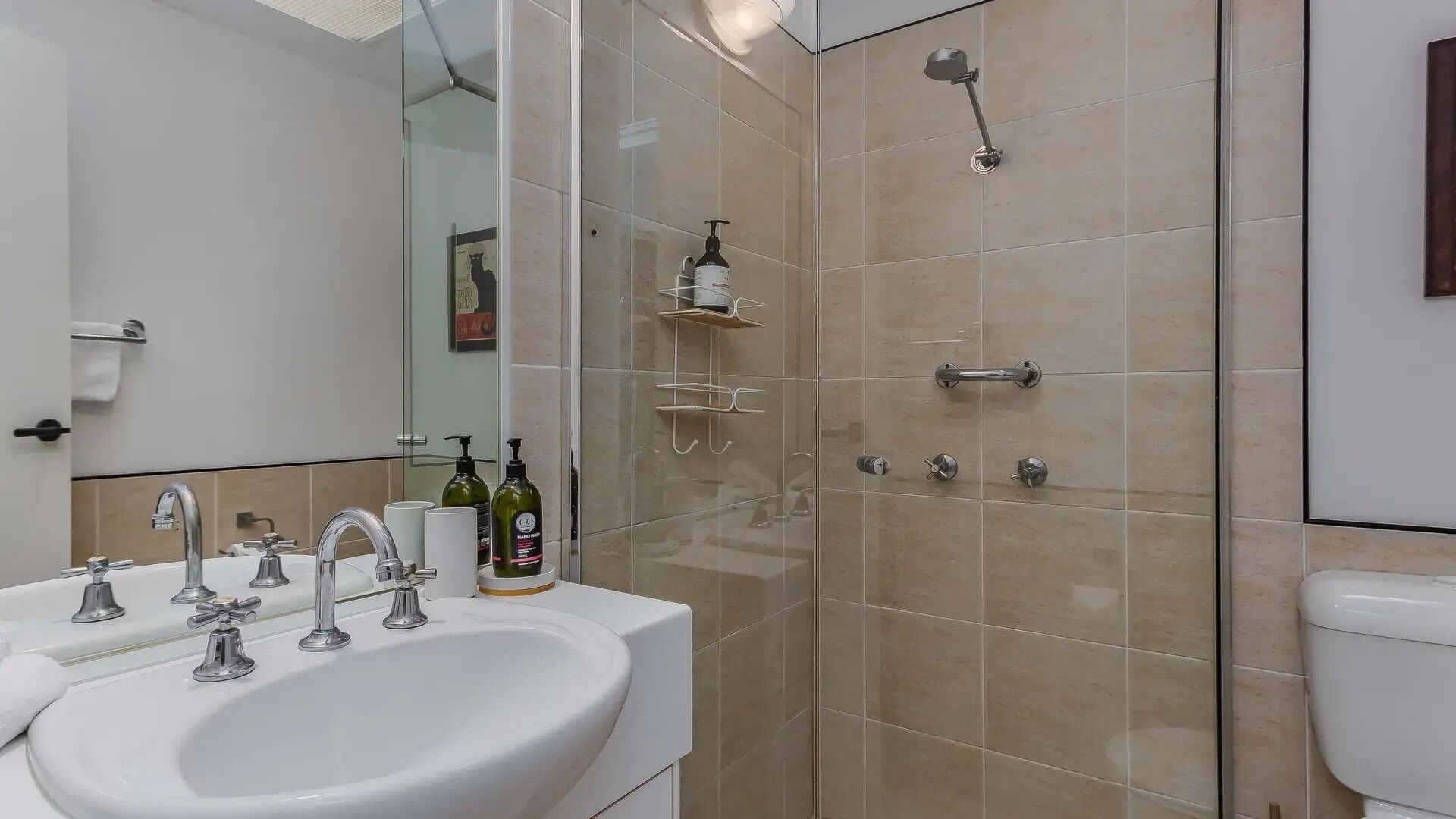 A bathroom with a white sink, multiple faucets, a glass shower enclosure, and a toilet.