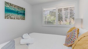 Ein Schlafzimmer mit Bett, einem Fenster mit Jalousien, einem Gemälde und einem Kopfkissen.