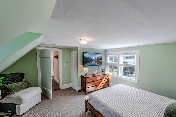 A bedroom with a bed, a dresser, a painting, and a window.