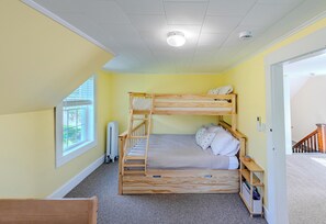 A bunk bed room with a window, a radiator, and a door leading to another room.