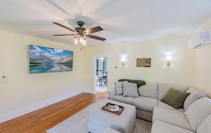 A living room with a ceiling fan, a large landscape painting, a sofa, and a dining area in the background. - Modernized Historic Mountain Getaway (Littleton)